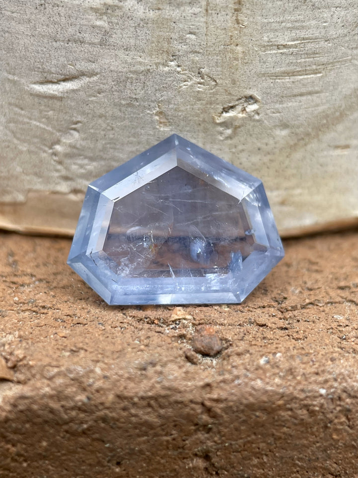 Sapphire resting on a rustic brick surface, highlighting its unique custom shield step cut and untreated seafoam, teal, and blue colors.