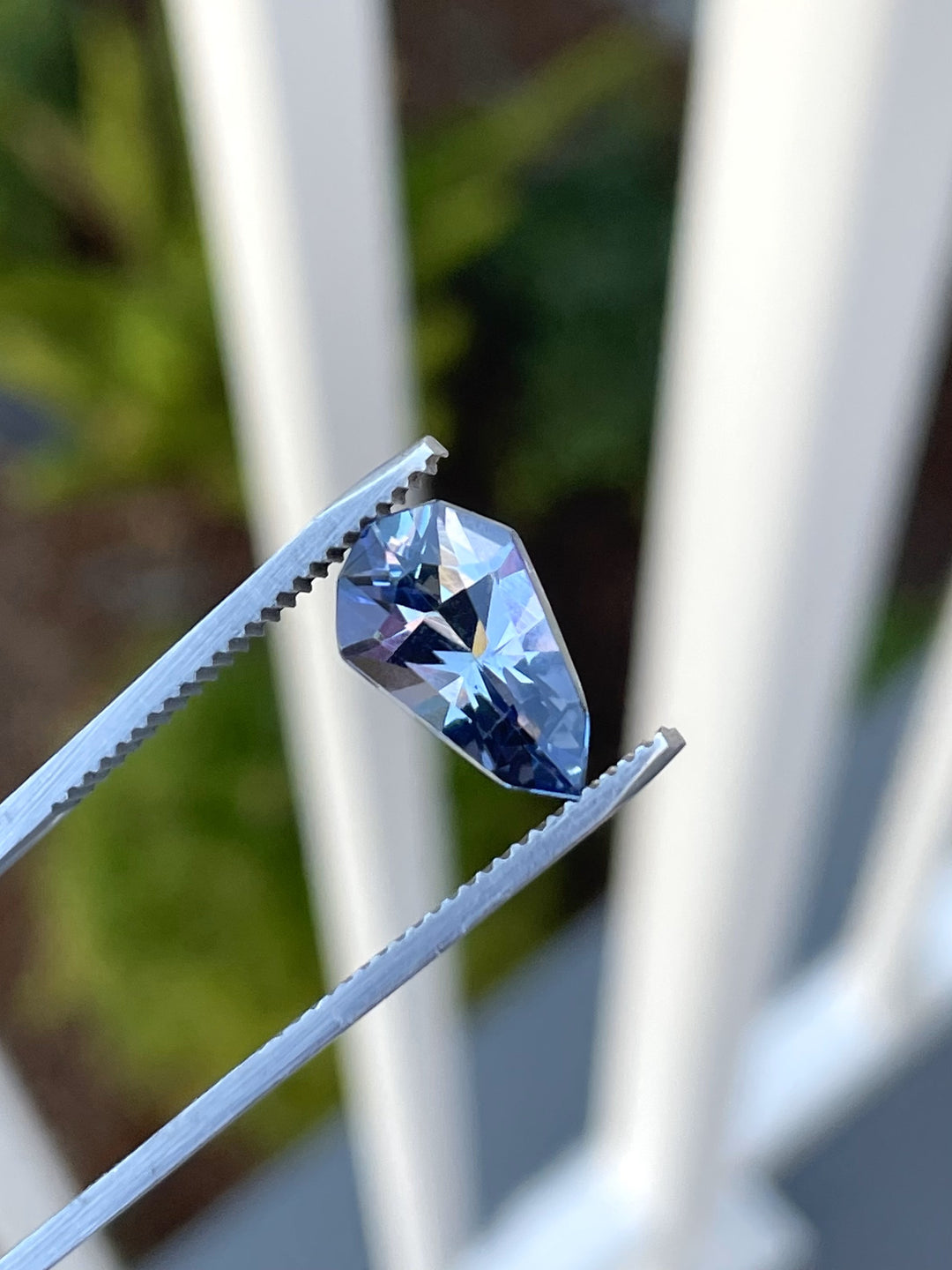 A 3.31-carat tanzanite gemstone featuring a unique mix of gray, blue, and purple hues in a modified geometric pear cut, elegantly displayed with precision tweezers.