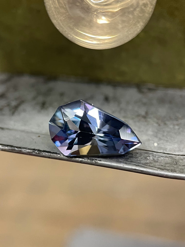 Close-up of a 3.31-carat Tanzanite gemstone with a stunning blend of gray, blue, and purple hues. Features a unique modified geometric pear cut, ethically sourced from the Merelani Hills in Tanzania.