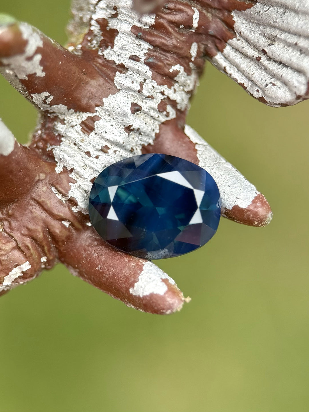 Brilliant oval-cut Nigerian sapphire with peacock tones photographed on a decorative surface to highlight its deep teal brilliance.