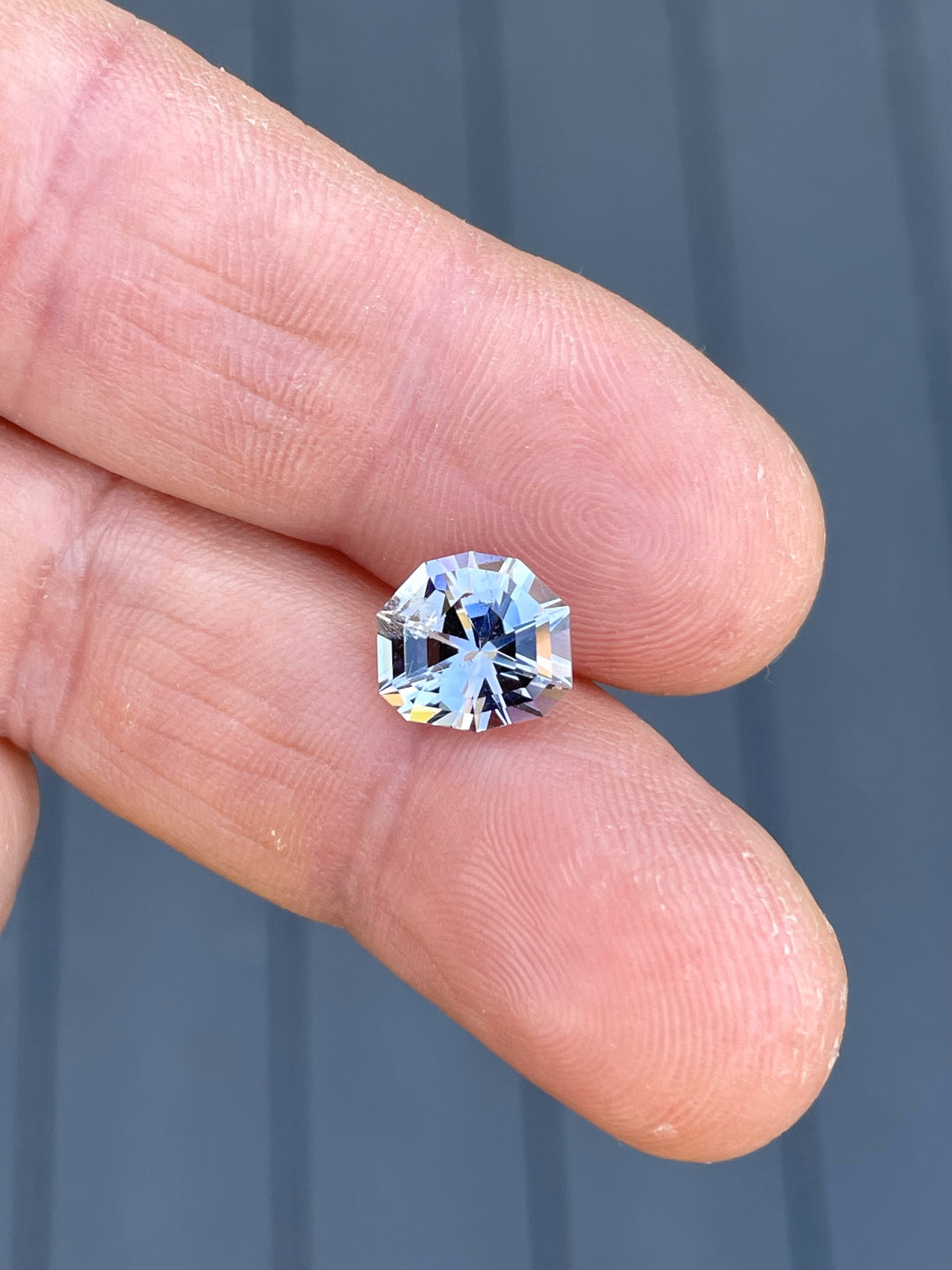 Hand holding a 3.33-carat Tanzanite gemstone with mermaid, gray, pink, and lavender hues in a custom mix step cut shield shape, sourced from Merelani Hills, Tanzania