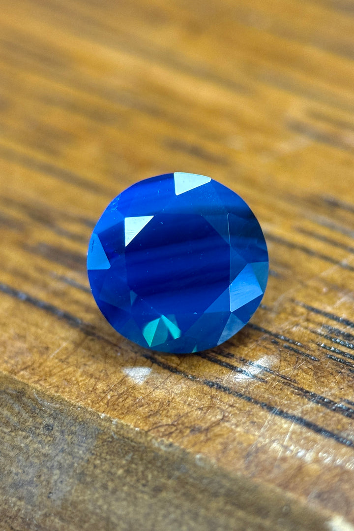 Faceted blue gemstone on a wooden surface