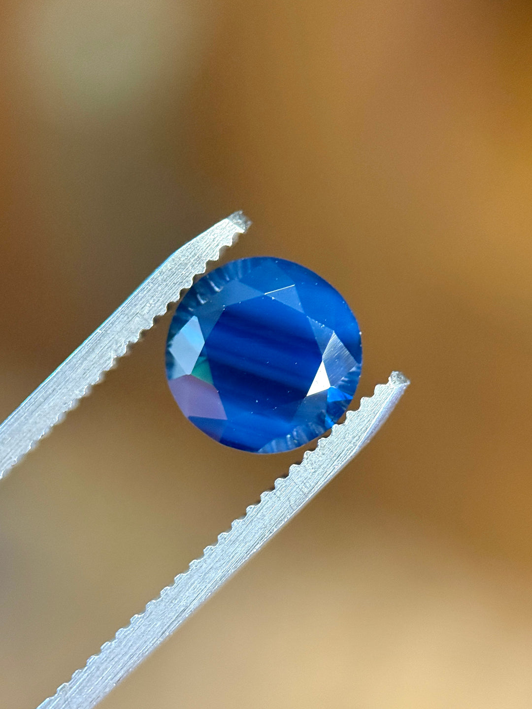 Blue gemstone held between tweezers against a blurred background