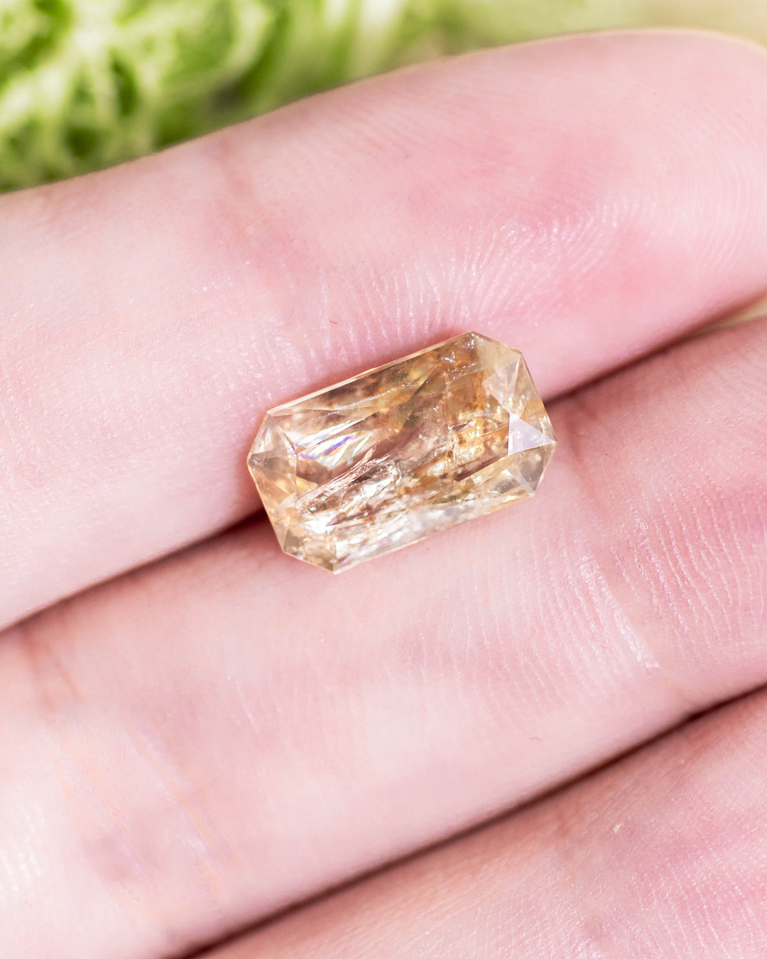 3.50 carat yellow orange sapphire displayed on fingertip under natural sunlight, highlighting elongated radiant cut symmetry and natural color zoning in this untreated gemstone from Umba River Valley, Tanzania.