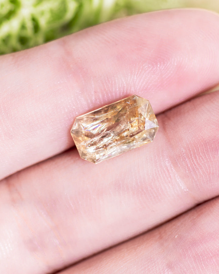 3.50 carat yellow orange sapphire displayed on fingertip under natural sunlight, highlighting elongated radiant cut symmetry and natural color zoning in this untreated gemstone from Umba River Valley, Tanzania.