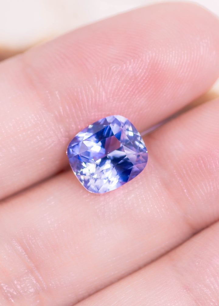 Loose gradient cornflower blue sapphire resting on a hand displaying the elongated cushion mixed cut and the soft cornflower blue tones in natural light.