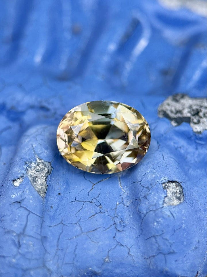 Macro photo of 3.70ct untreated Tanzanite in peach, teal, and golden yellow, placed on textured blue background