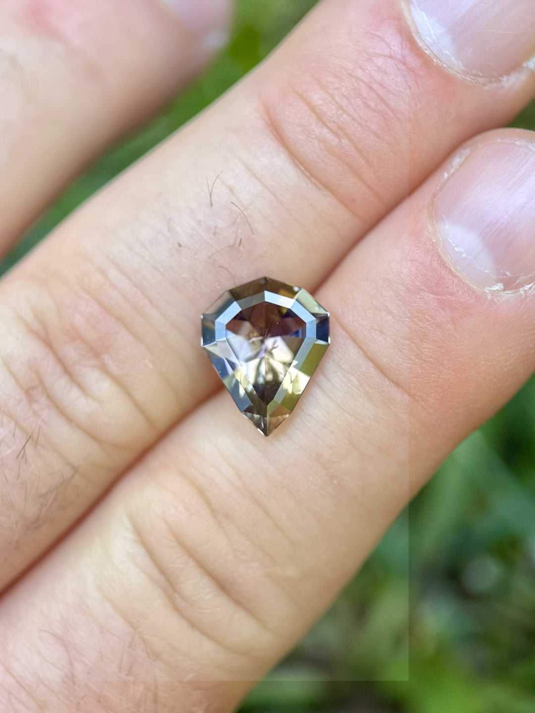 3.74 carat Tanzanite gemstone in custom shield mixed cut held in hand with vibrant peach, orange, and purple tones