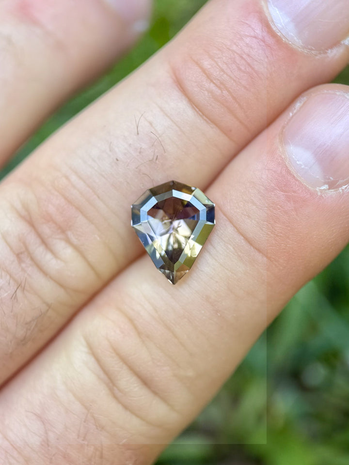 3.74 carat Tanzanite gemstone in custom shield mixed cut held in hand with vibrant peach, orange, and purple tones