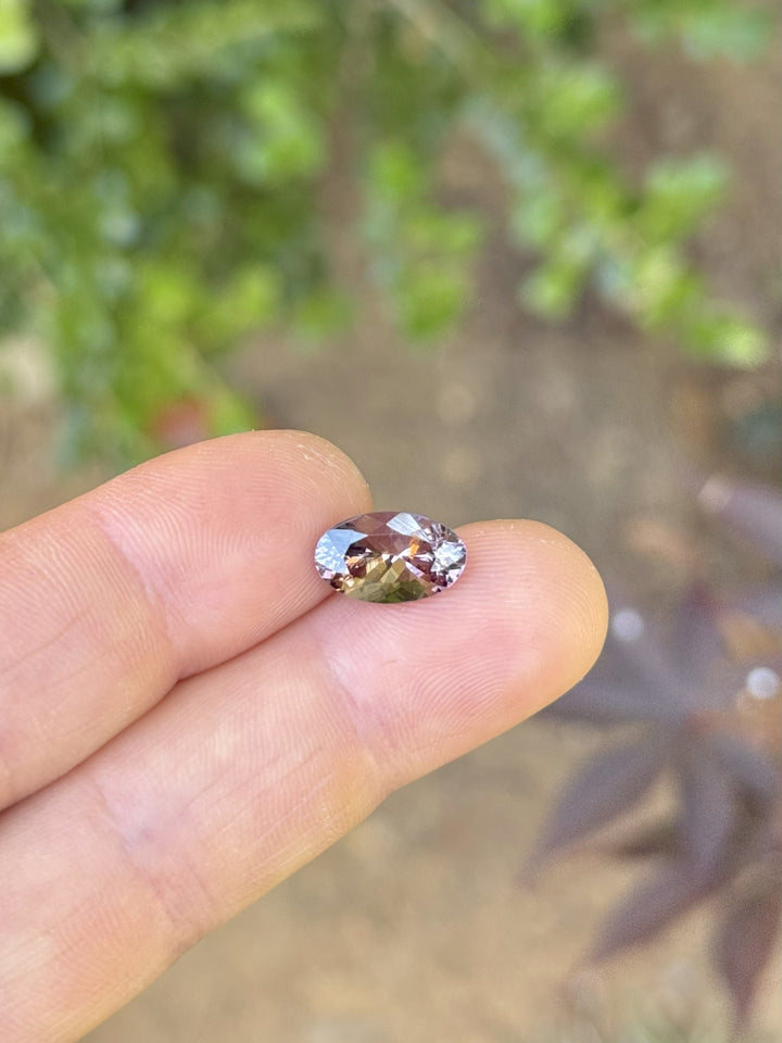 Oval reddish orange tanzanite resting on fingertips, showing vibrant sparkle in natural daylight