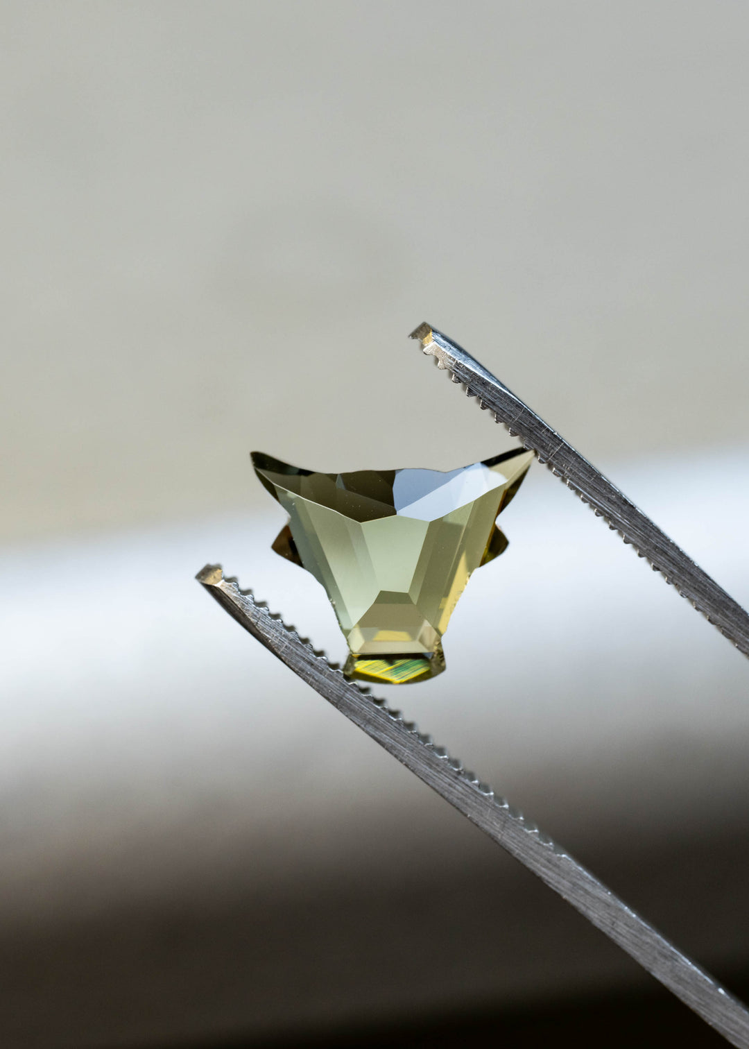Natural green and yellow Tanzanite held in tweezers showing the precision El Toro custom cut and unique geometric faceting.