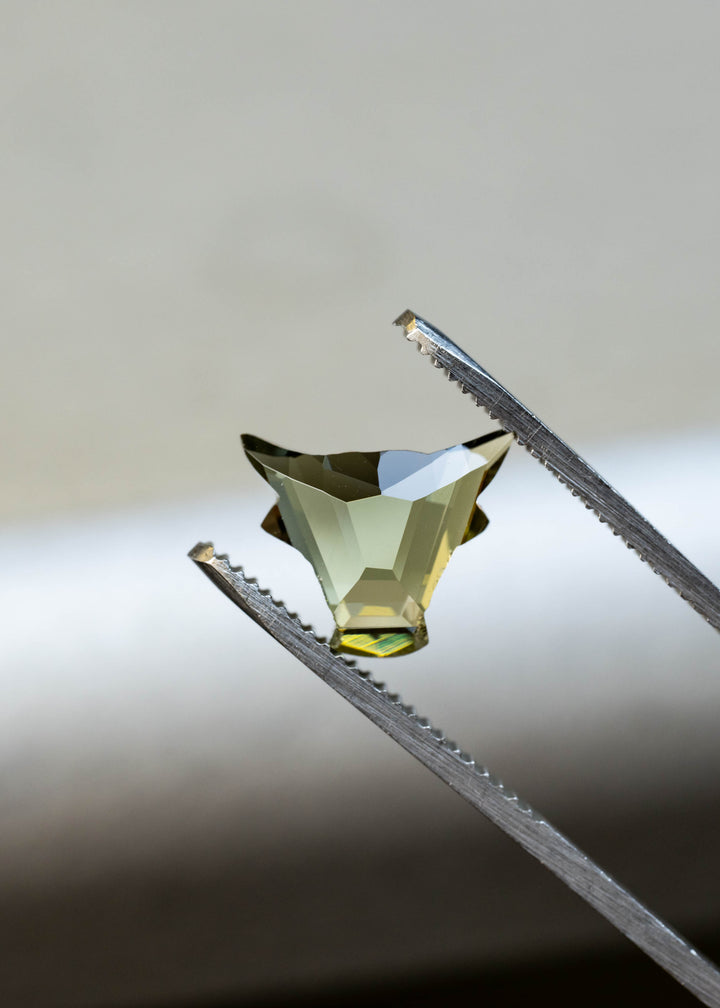 Natural green and yellow Tanzanite held in tweezers showing the precision El Toro custom cut and unique geometric faceting.