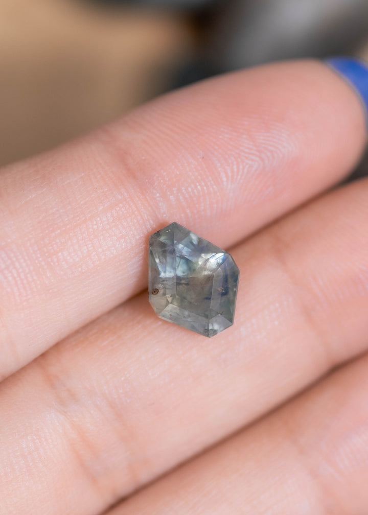 3.78ct Montana teal sapphire resting on fingertips, highlighting its substantial depth, kite silhouette, and shifting blue-green tones with subtle internal feathering.