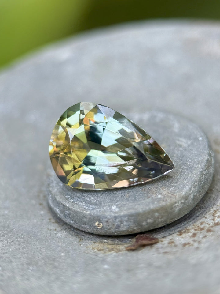 3.80ct pear-cut Tanzanite gemstone resting on natural texture, displaying purple, green, and teal mermaid hues