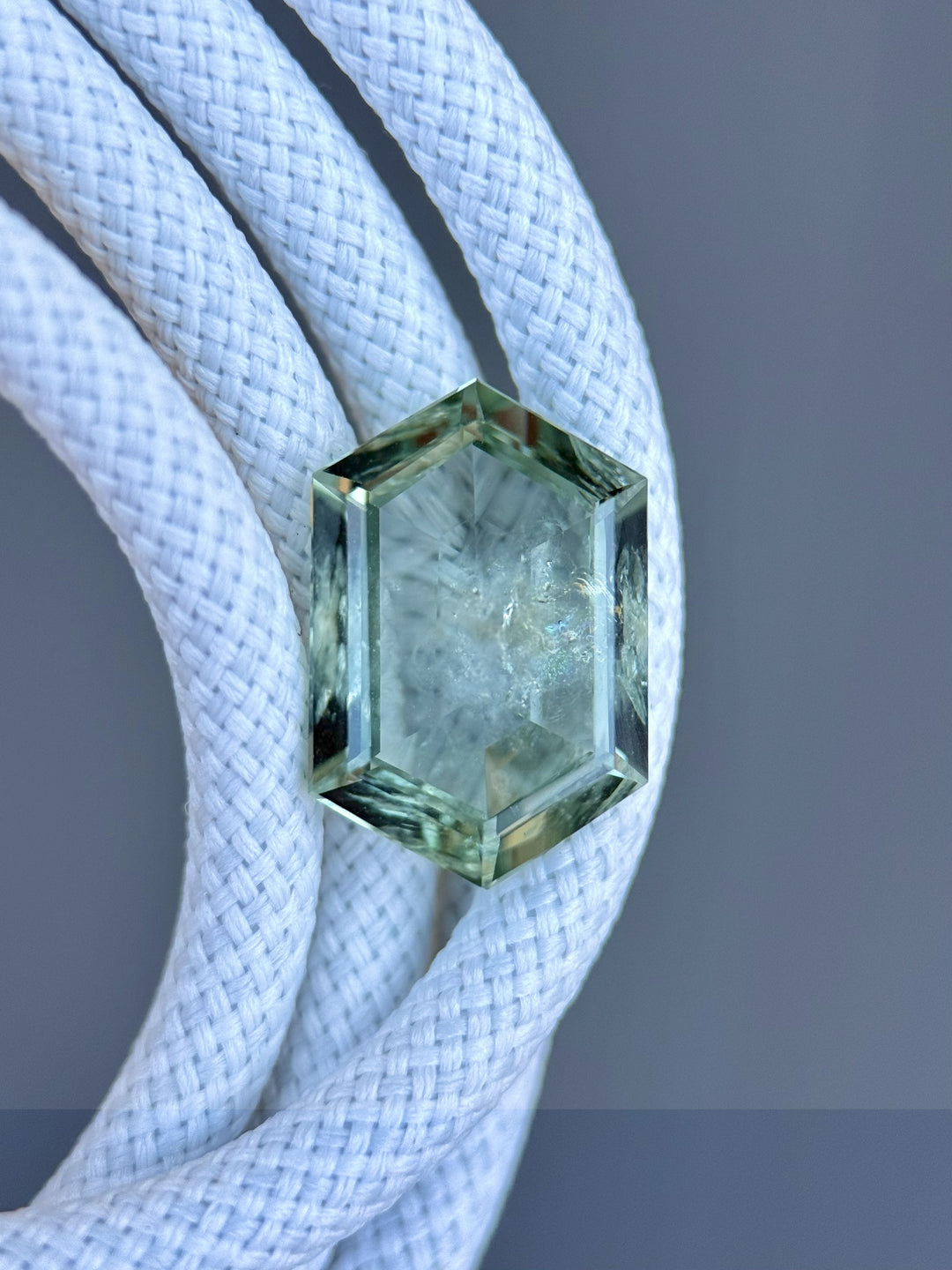 Close-up of untreated teal green hexagon sapphire from Montana resting on braided white rope