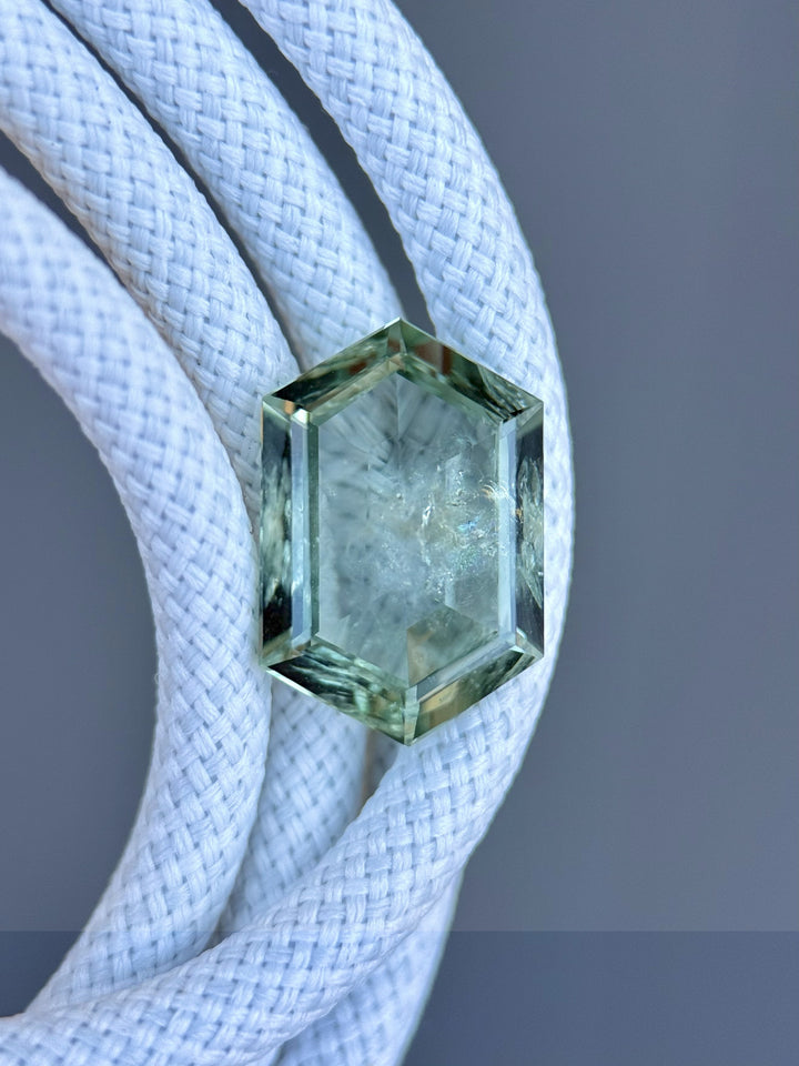 Close-up of untreated teal green hexagon sapphire from Montana resting on braided white rope