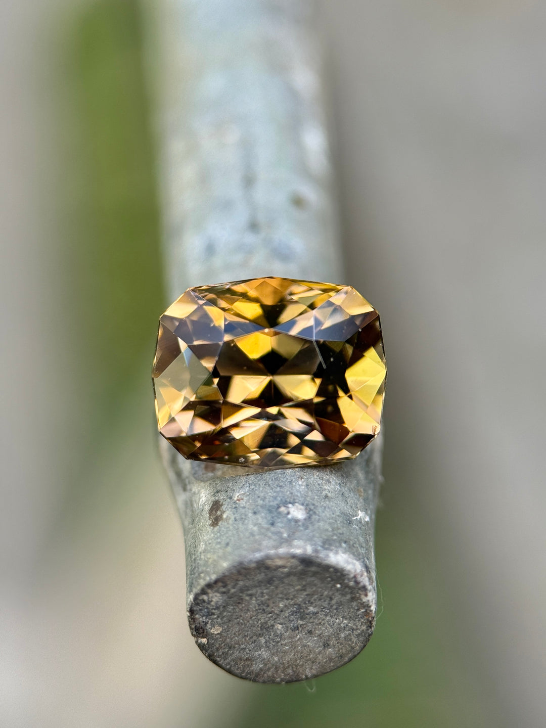 3.81 carat Tanzanite gemstone resting on a metal rod, displaying fancy tones of lavender, pink, and golden yellow with exceptional sparkle from its custom geometric cushion modified brilliant cut, untreated natural gem from Merelani Hills, Arusha Region, Tanzania.