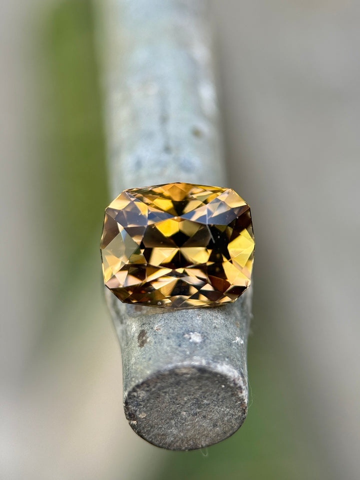 3.81 carat Tanzanite gemstone resting on a metal rod, displaying fancy tones of lavender, pink, and golden yellow with exceptional sparkle from its custom geometric cushion modified brilliant cut, untreated natural gem from Merelani Hills, Arusha Region, Tanzania.