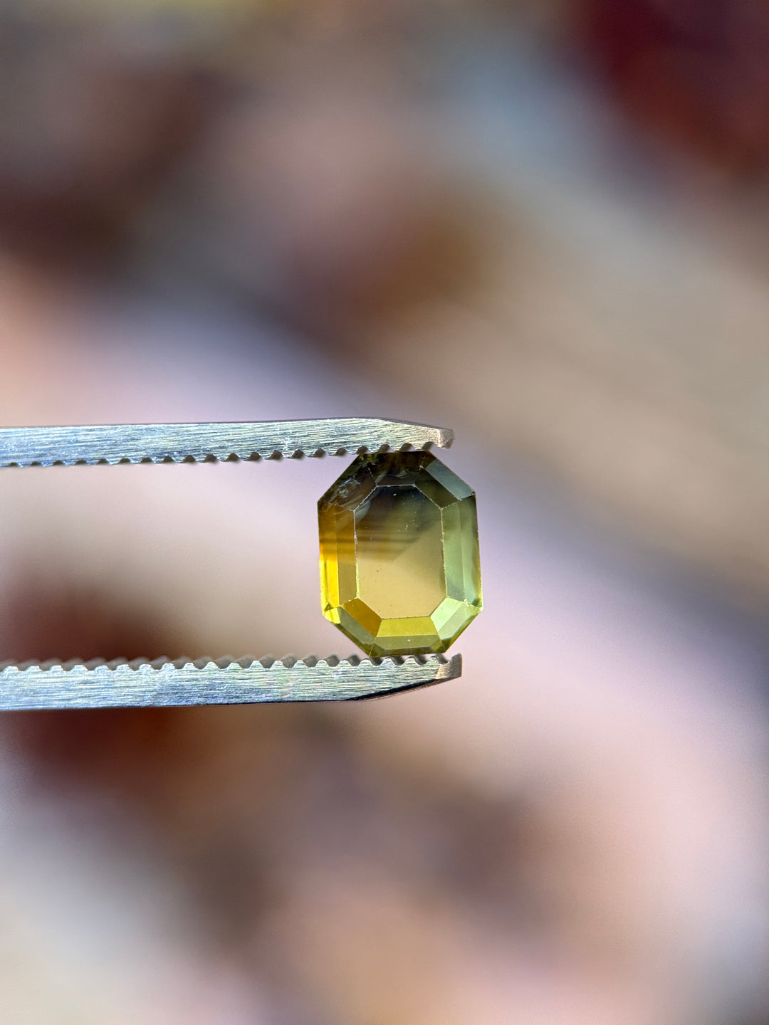 Loose antique cut sapphire with yellow and grey parti color zoning held in gem tweezers