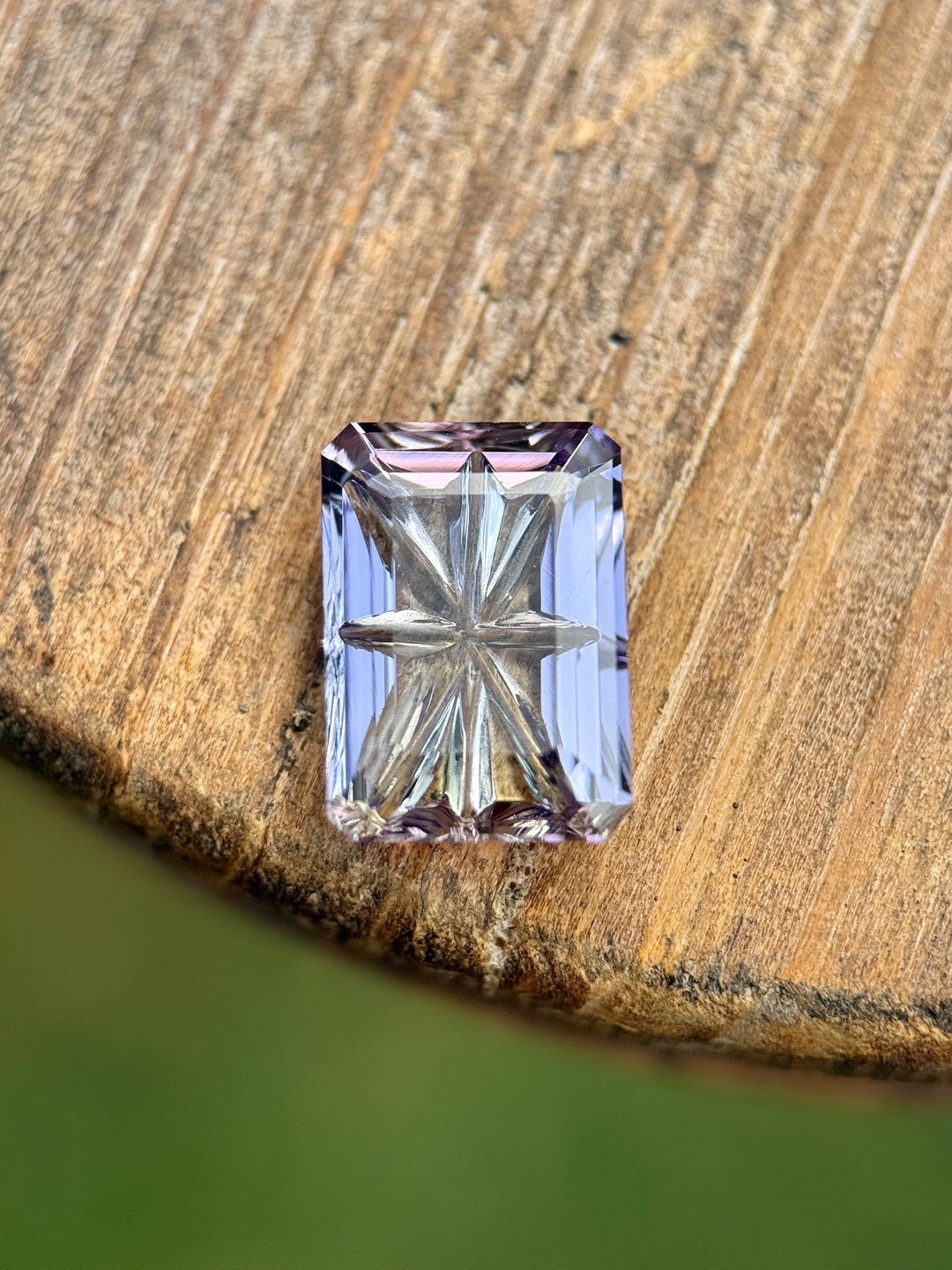 Multi-color Tanzanite weighing 4.01 carats displayed on wood surface, showing blue, pink, and purple hues with a custom concave fantasy emerald cut. Detailed portrait cut pattern visible; untreated Tanzanite from Merelani Hills.