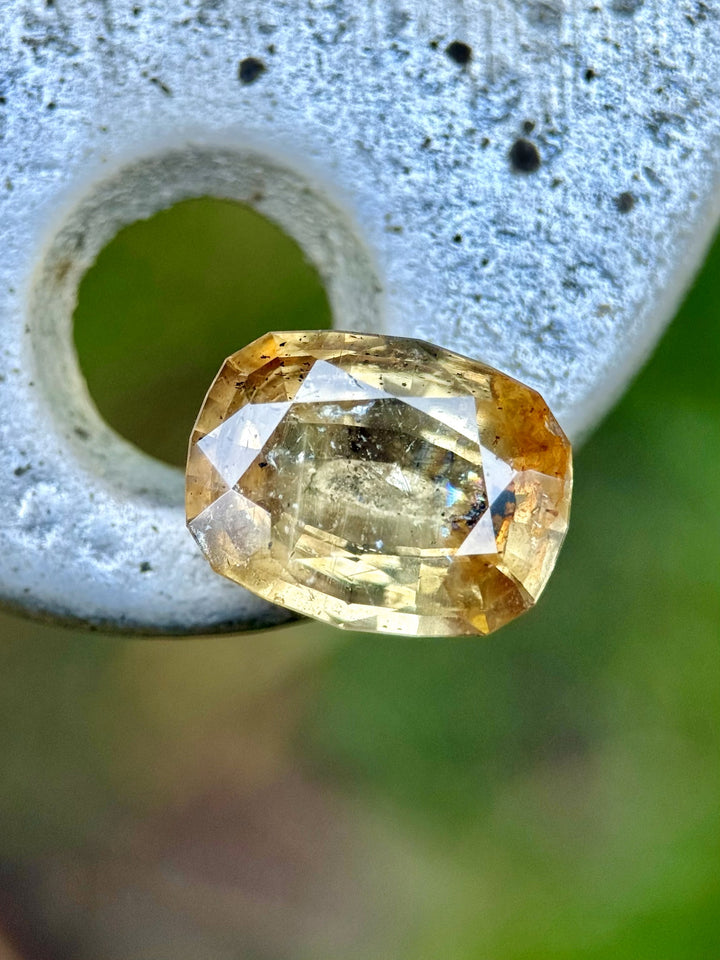 Close-up of a 4.02-carat sapphire in a custom antique cushion cut, displaying earthy greenish pinkish golden peach tones with visible orange fluorescence, sourced from Umba River, Tanzania.