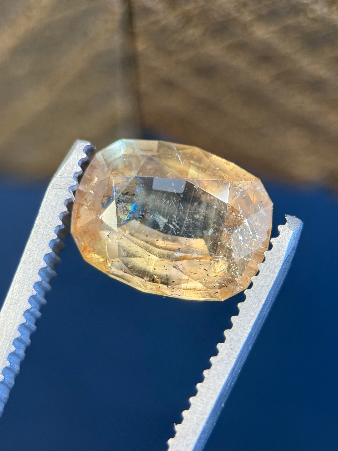 4.02-carat untreated sapphire held in tweezers, reflecting a mix of golden, peach, and green tones with vibrant internal texture and sparkle.
