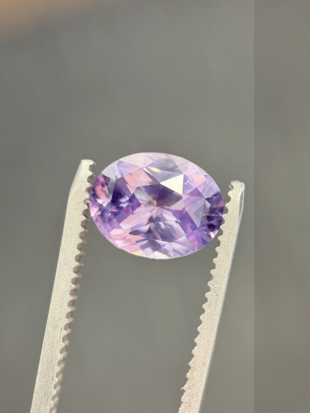 Violet to pink color change sapphire, 4.04 carats, held in gem tweezers against a neutral background to reveal precision faceting and natural brilliance, ethically sourced from Sakaraha, Madagascar.