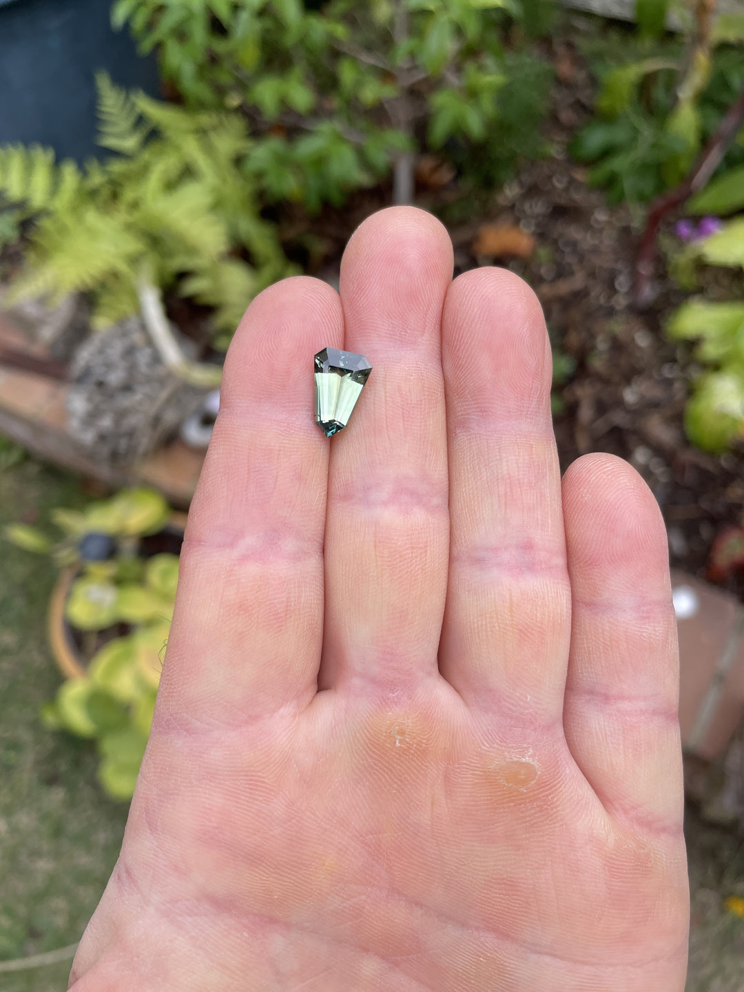 4.07 carat untreated sapphire resting on a palm, showcasing a custom shield step cut and a captivating blend of blue, green, and teal.