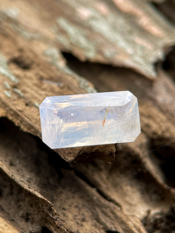 A 4.18-carat sapphire in opalescent white and yellow hues, placed on a natural wooden surface. The gem is cut in an elongated radiant shape with no treatments