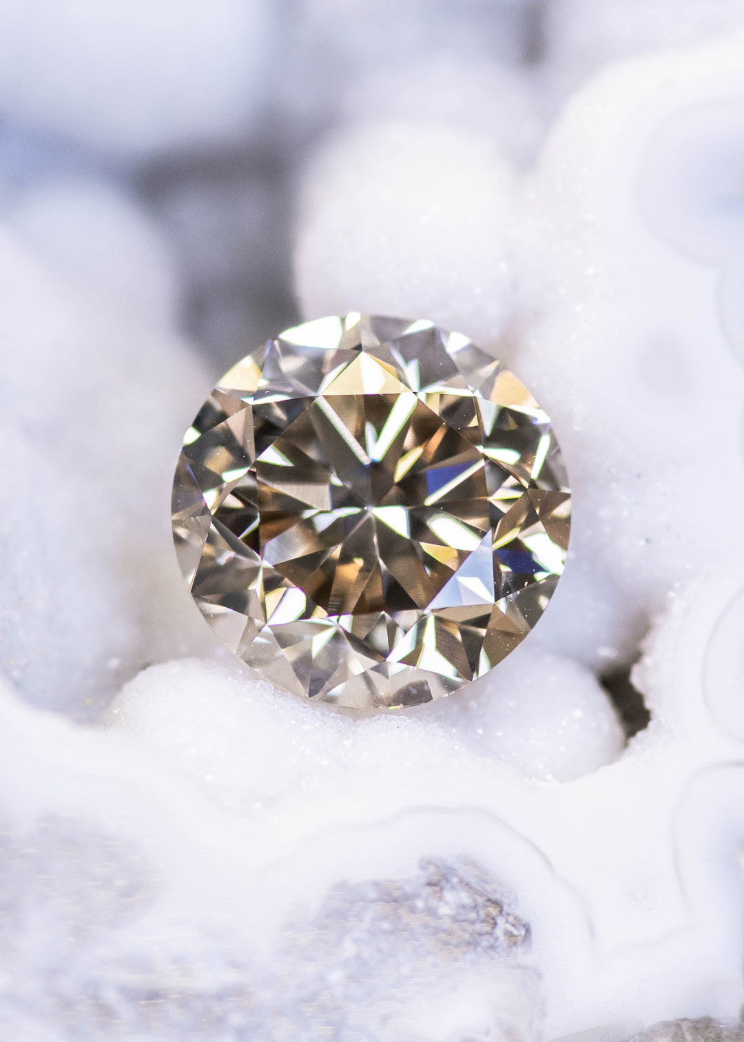 Round brilliant champagne diamond on textured white background, displaying bright scintillation and warm caramel reflections.