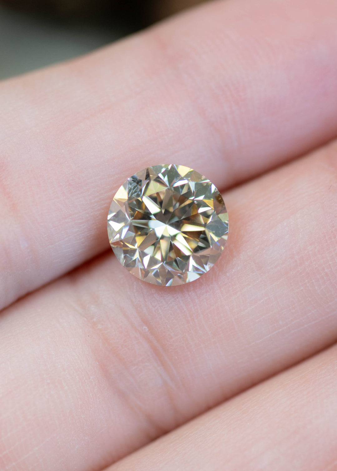 4.23ct champagne C3 round brilliant diamond resting on fingertips, showing warm golden-brown tones and strong brilliance.