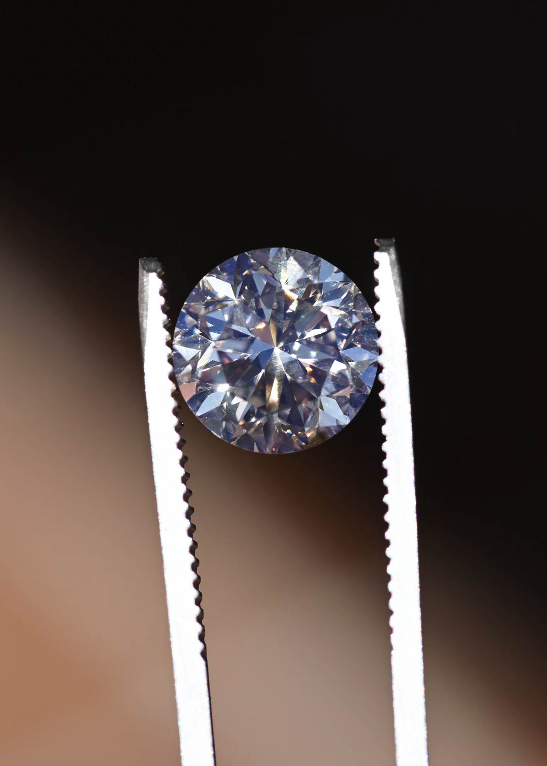 Canadian C3 champagne diamond held in tweezers, highlighting excellent symmetry and crisp round brilliant faceting.