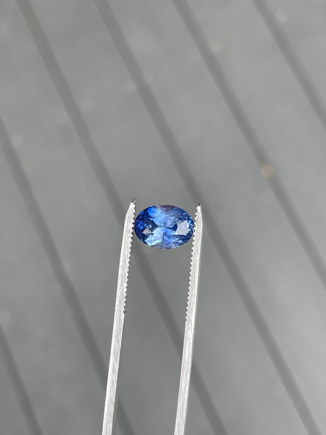 A stunning 4.51-carat cornflower blue sapphire, held in precision tweezers against a neutral gray background, showcasing its brilliant oval cut and Sri Lanka origin.
