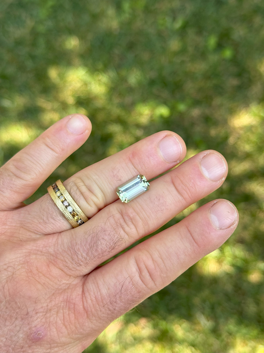 4.51 carat mint green tourmaline resting across fingertips in natural light, showing its elongated emerald cut brilliance and soft green hue, untreated gemstone sourced from Congo, Africa.