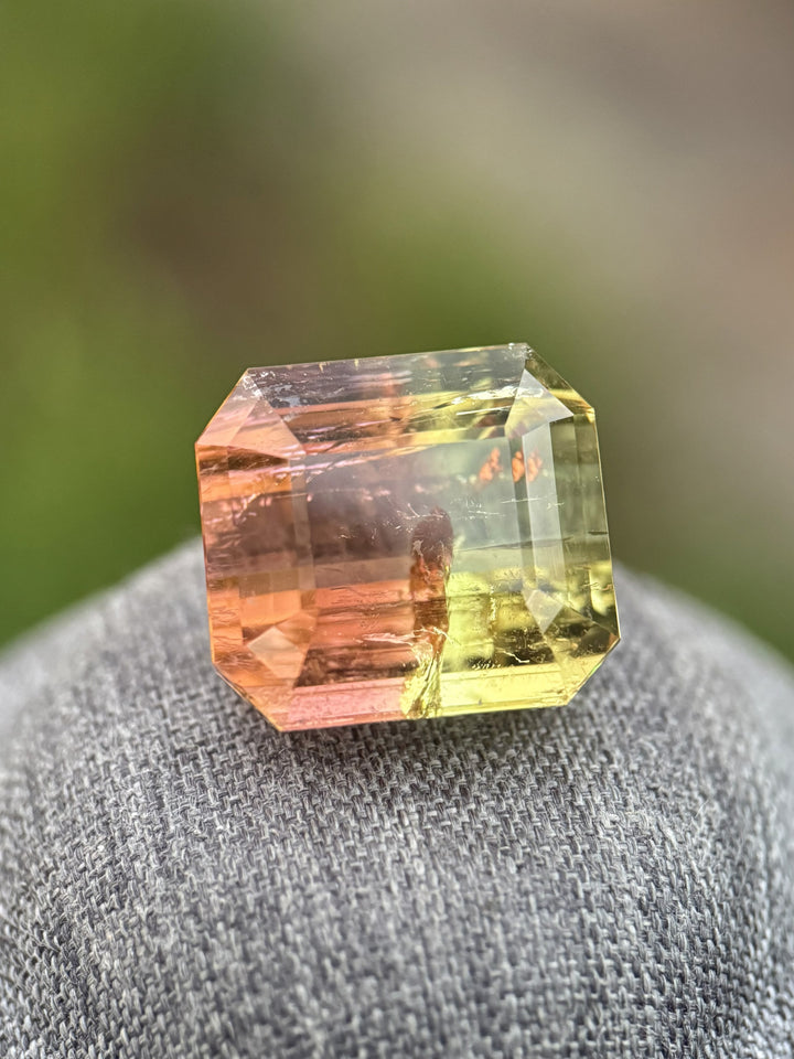 43.06 carat multi color tourmaline resting on fabric surface, emerald cut from Mozambique showing yellow green orange pink peach color zoning and step faceting