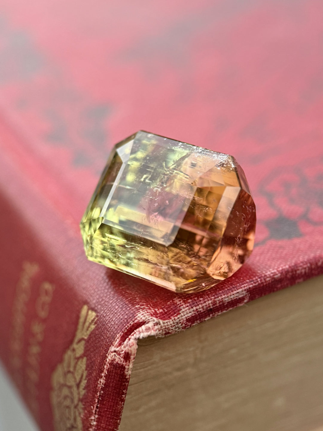43.06ct emerald cut tourmaline displayed on vintage book, Mozambique origin gemstone with yellow green to peach pink bi color transition