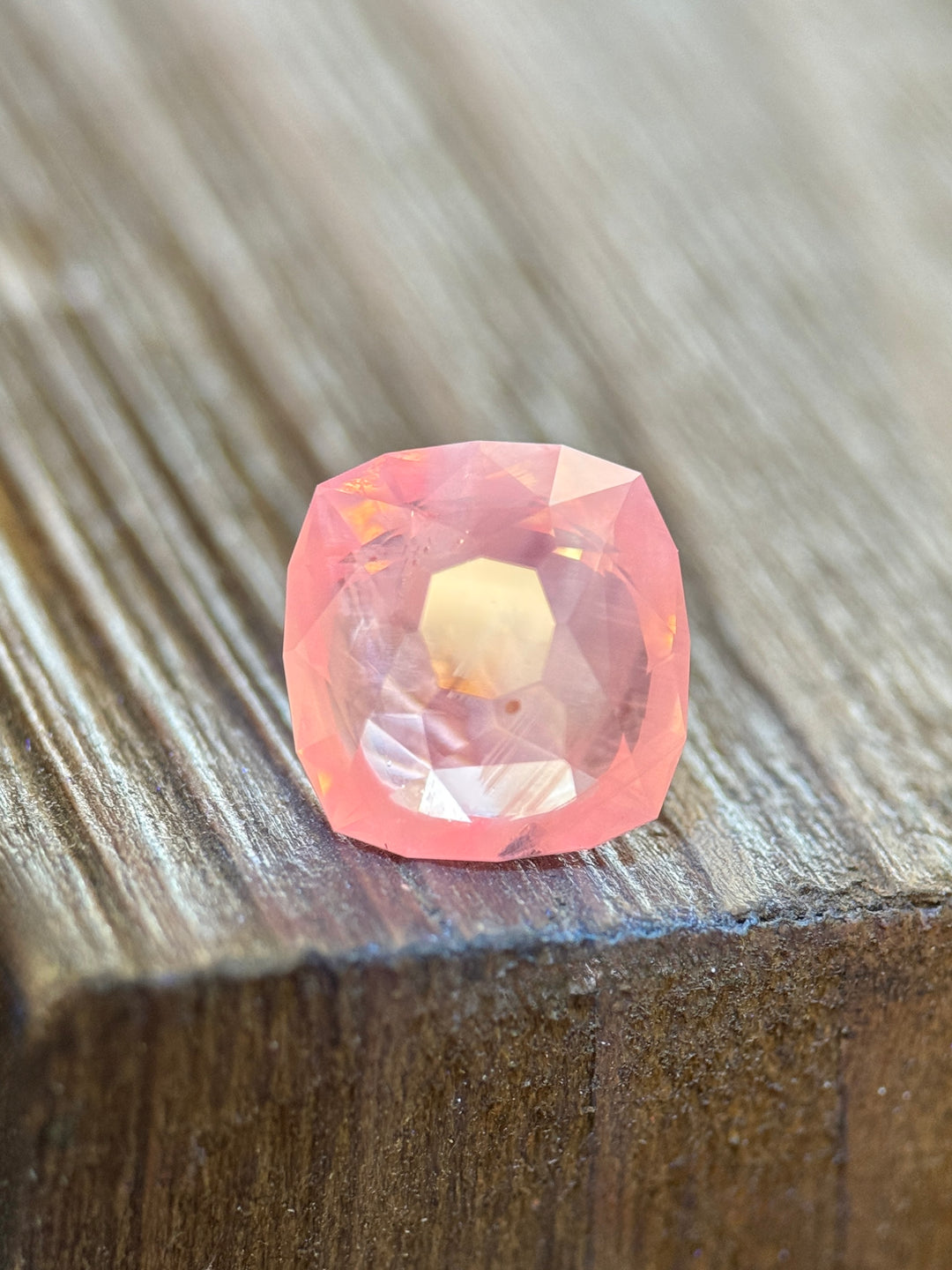 Light pink opalescent sapphire displaying bring pink fluorescence on wooden surface.