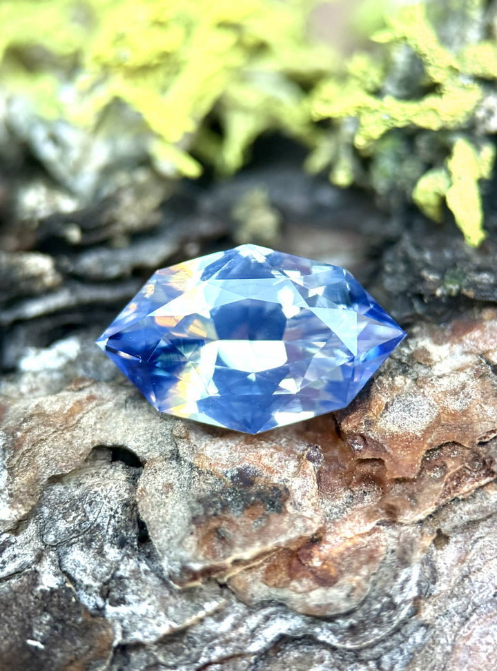 5.00 carat blue white parti sapphire resting on textured bark, showing the opalescent reflections and color zoning of the precision custom marquise mixed cut, untreated sapphire from Sakaraha, Madagascar.