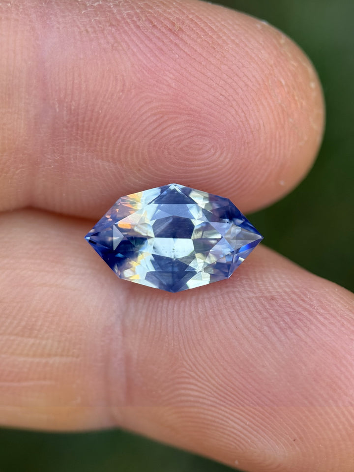 5.00 carat parti blue and white sapphire displayed on fingertips under natural sunlight, revealing the gemstone’s precision marquise mixed cut and the contrast of icy blue and white color zoning, untreated sapphire from Sakaraha, Madagascar.