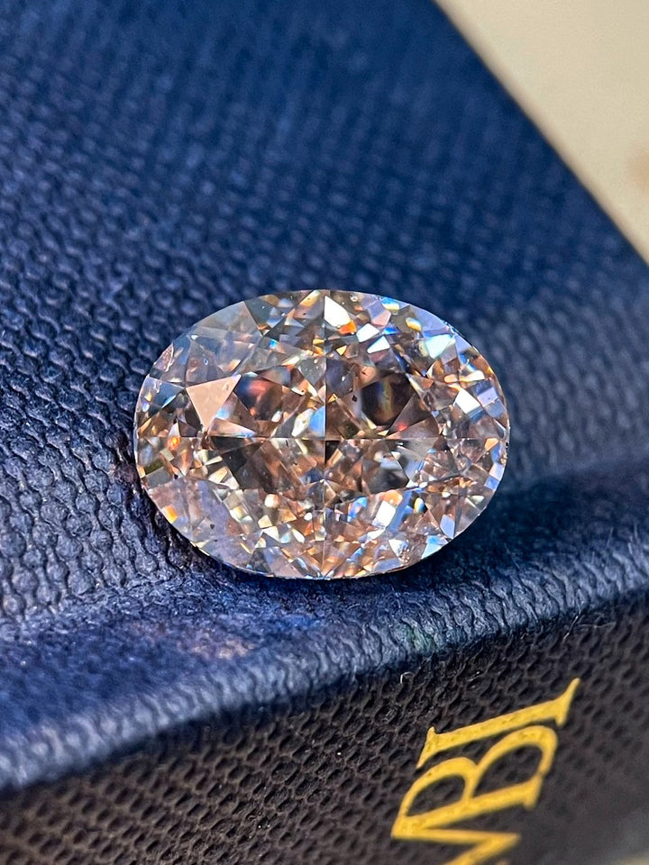 5.25 Carat Light Champagne Diamond with Strong Rosiness displayed on a textured blue surface, highlighting its dazzling facets and brilliance.