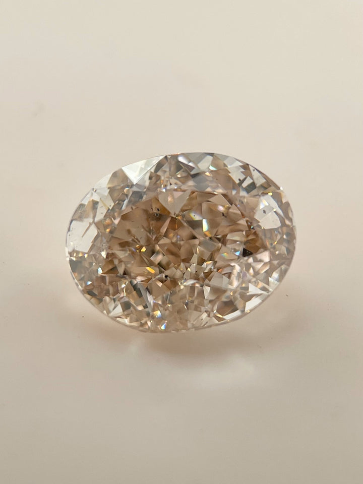 Close-up of a 5.25-carat oval brilliant champagne diamond showcasing strong rosiness and light champagne hues, placed on a neutral background. The diamond exhibits exceptional sparkle and strong blue fluorescence.