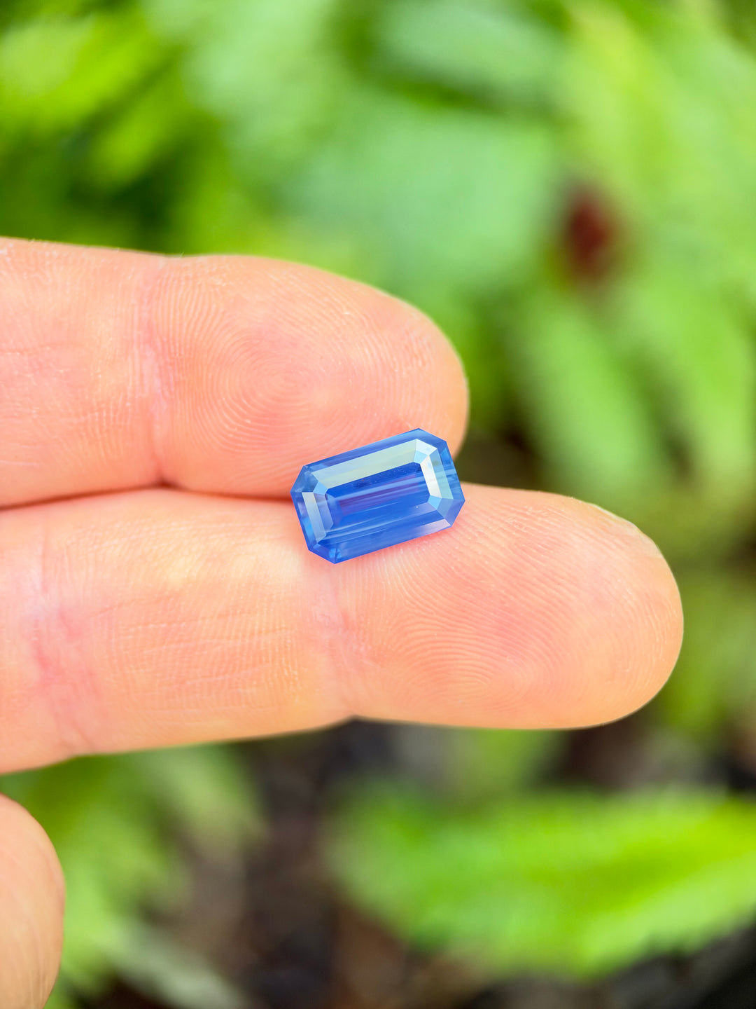 5.30 carat opalescent blue sapphire shown on hand for scale, precision cut in an elongated emerald shape