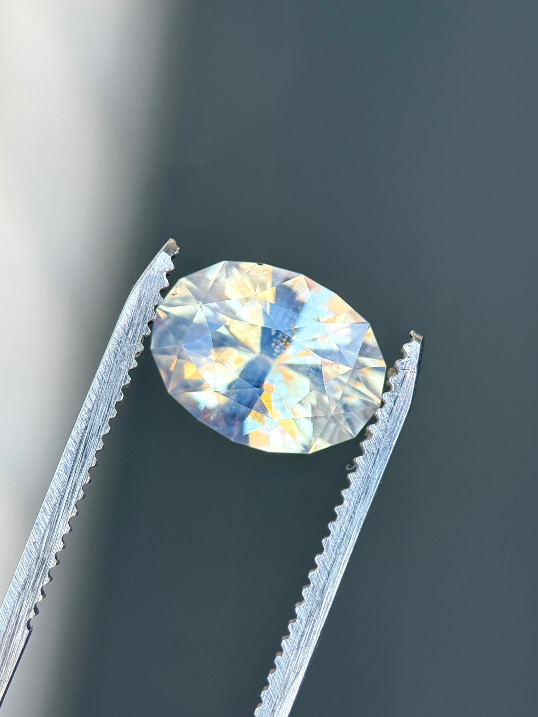 5.56 carat seafoam sapphire held in tweezers highlighting oval brilliant cut and opalescent character.