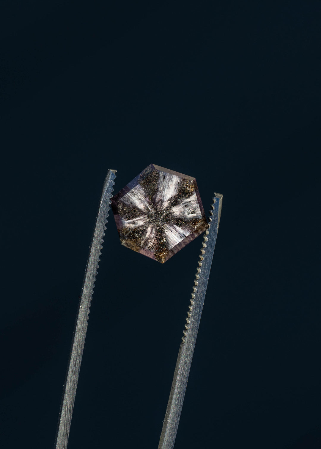 An untreated 5.56ct Afghan sapphire photographed against deep blue, emphasizing its lavender-purple transparency and natural black radial inclusions. The portrait cut preserves the stone's striking internal pattern.