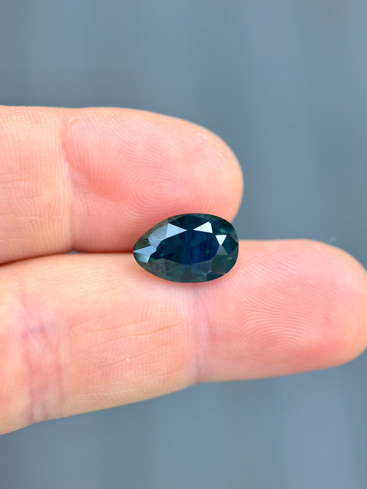 6.22 carat Nigerian sapphire on fingertip showing size scale and deep teal color saturation.