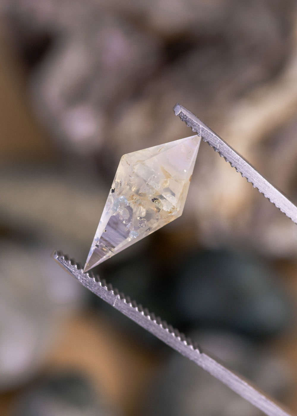 6.39ct untreated Sri Lankan sapphire held in tweezers, highlighting the faceted rhombohedral shape, earthy tones, faint silvery blue color, and natural inclusions