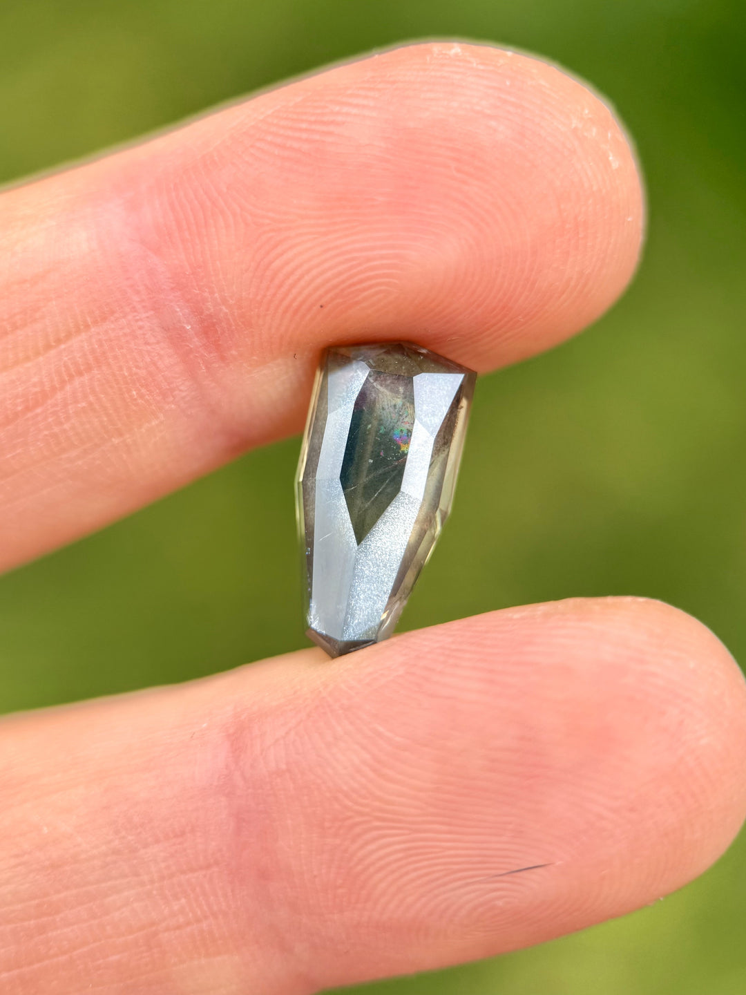 Hand holding a 6.74-carat color-changing bluish-green sapphire with custom elongated shield cut from Umba River, Tanzania
