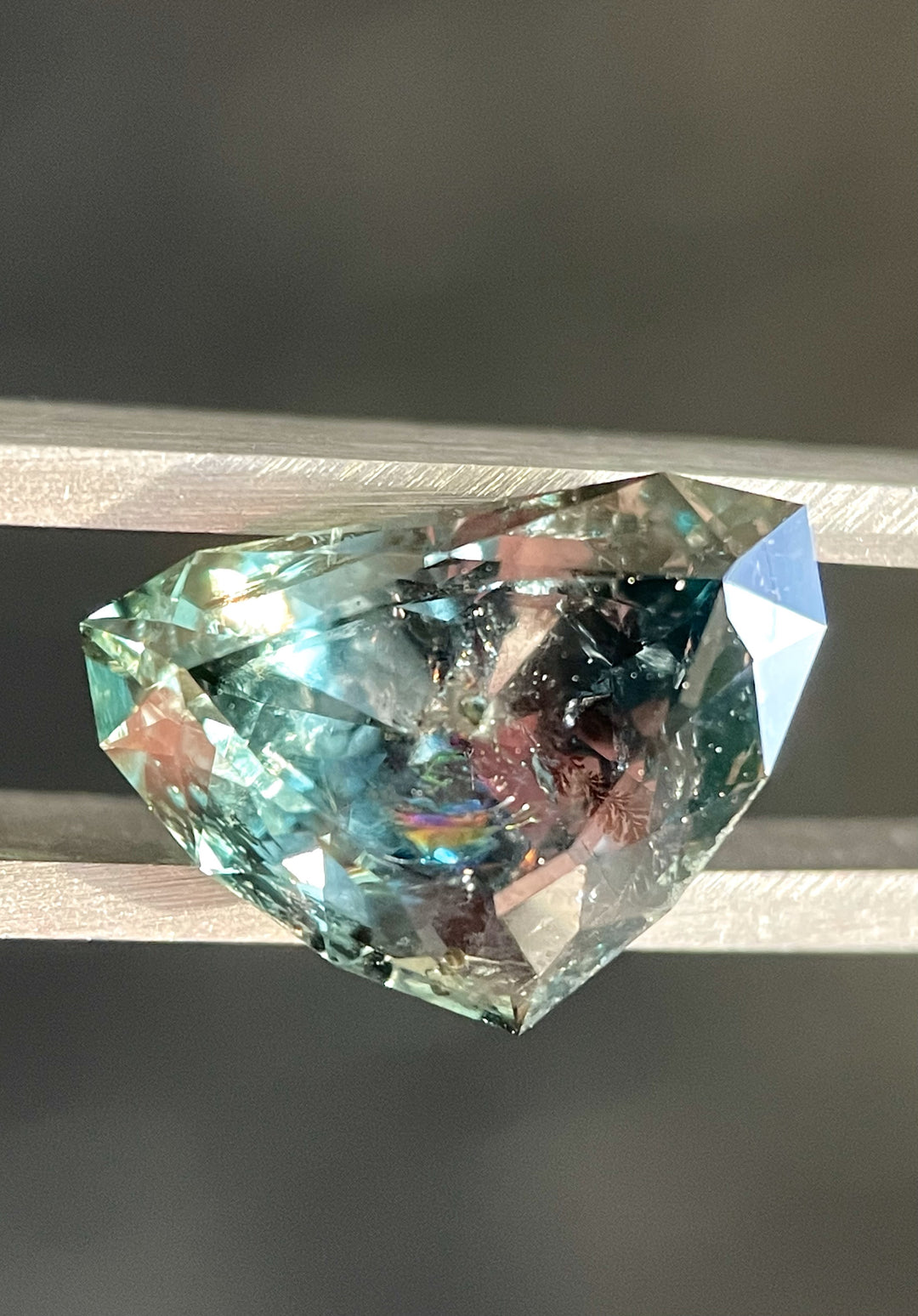 A close-up view of a 7.06-carat bluish-green sapphire transitioning to gray-purple, featuring a modified shield brilliant cut. Origin: Montana, untreated.
