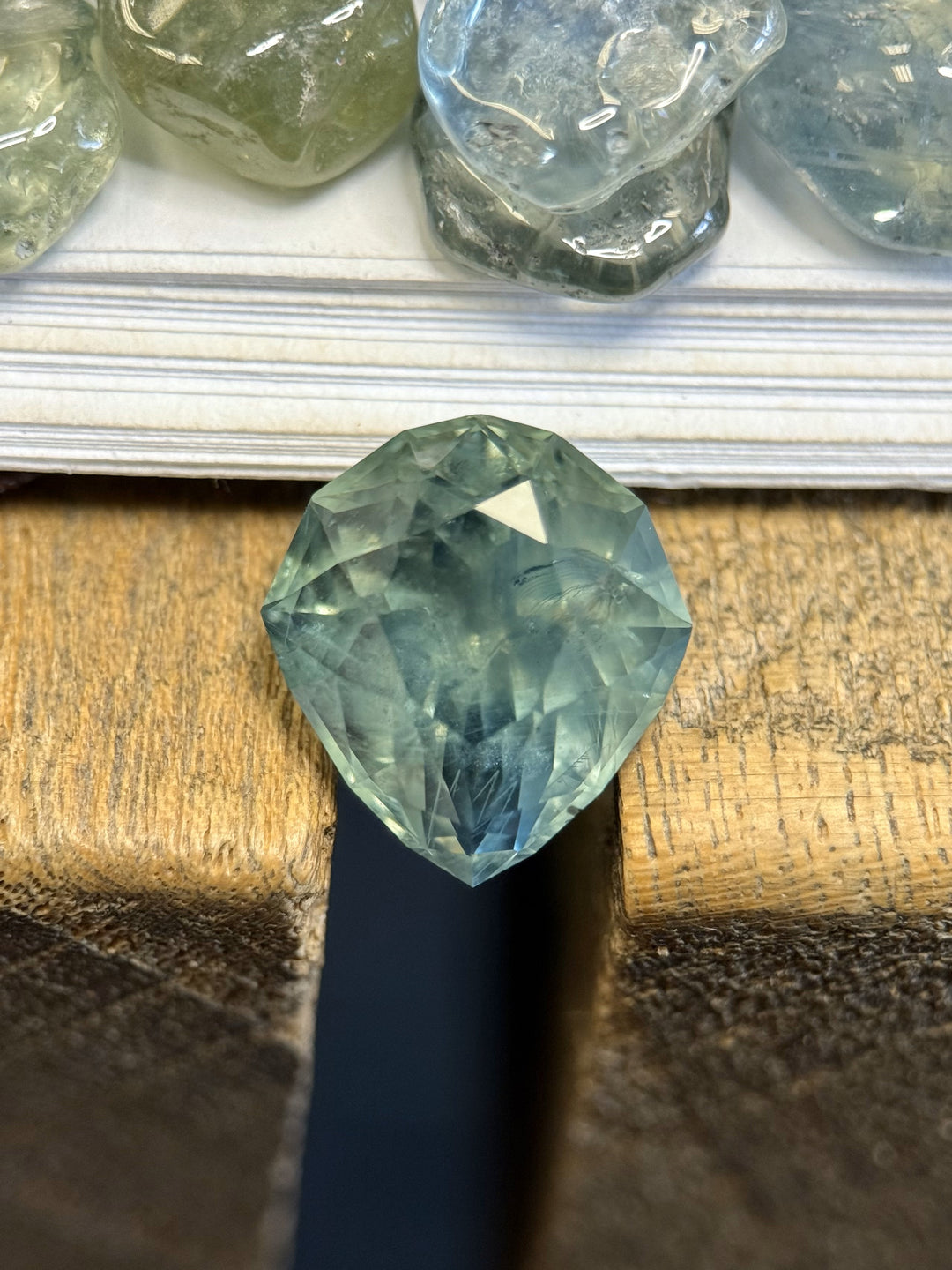 7.08ct custom geometric pear sapphire from Montana in silky blue, green, and teal hues, displayed on a wood background.