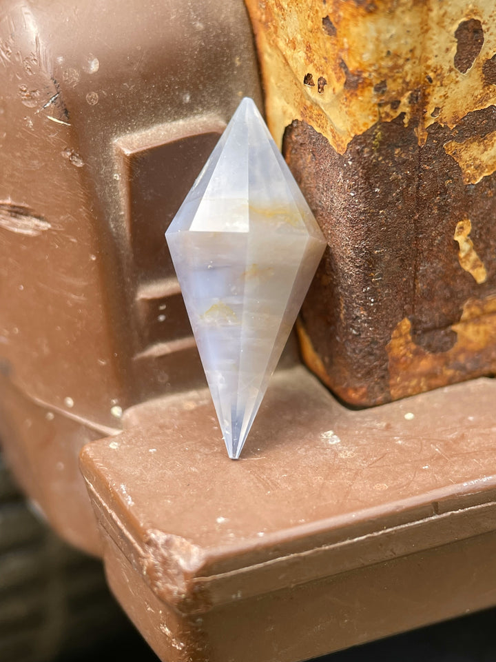 Faceted rhombohedral 8.00 carat sapphire from Sri Lanka with an earthy periwinkle hue, standing upright in a vertical position for dimension.